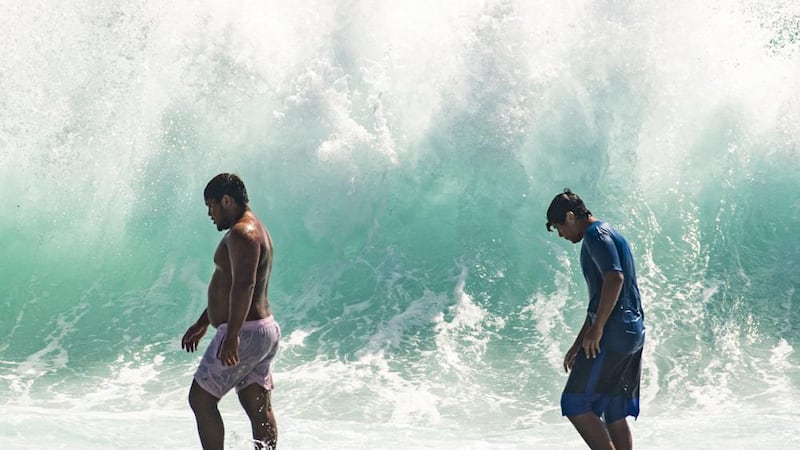 Dos personas caminan frente a olas gigantes cerca de Kapahulu Groin en el muro de Waikiki, Hawai.